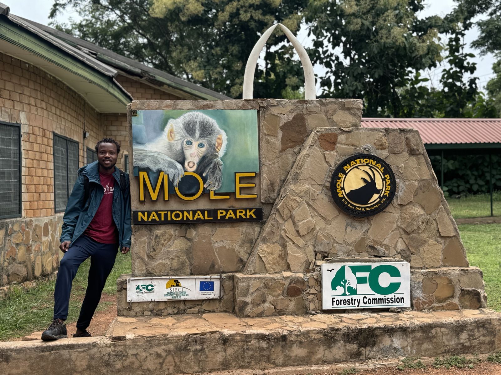 Samuel beside the entrance sign of Mole National Park, Ghana