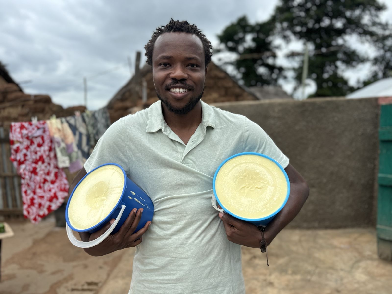 Samuel holding two tubs of shea butter in Murugu community